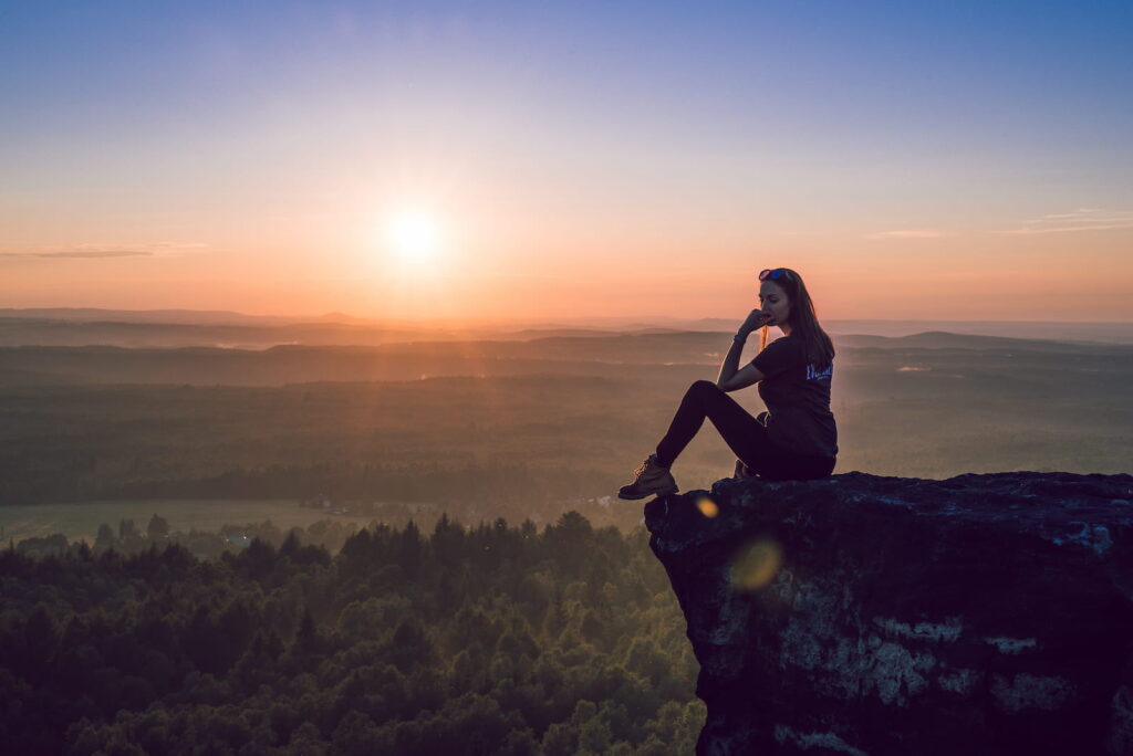 A woman sitting on a rock during colorful sunset.